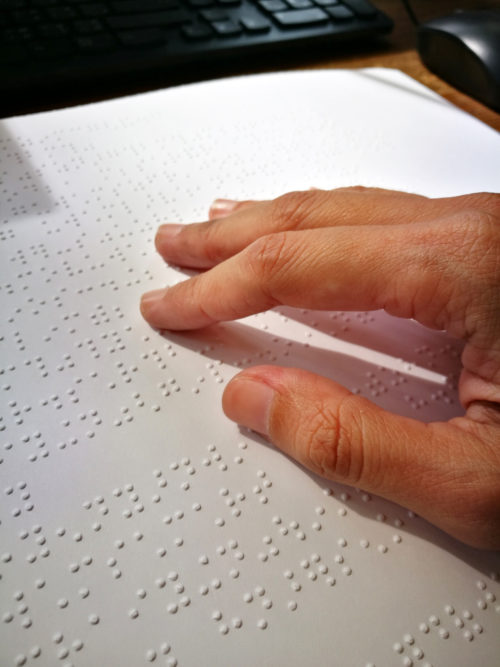 person reading braille with a keyboard and mouse in the background